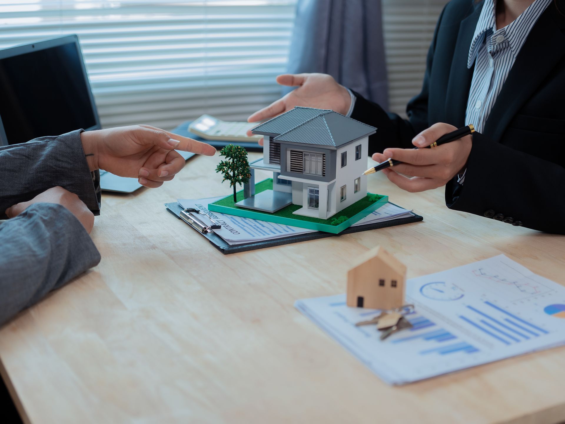 Deux personnes assises à un bureau examinent une maison témoin et des documents ; l'une d'elles prend une note.