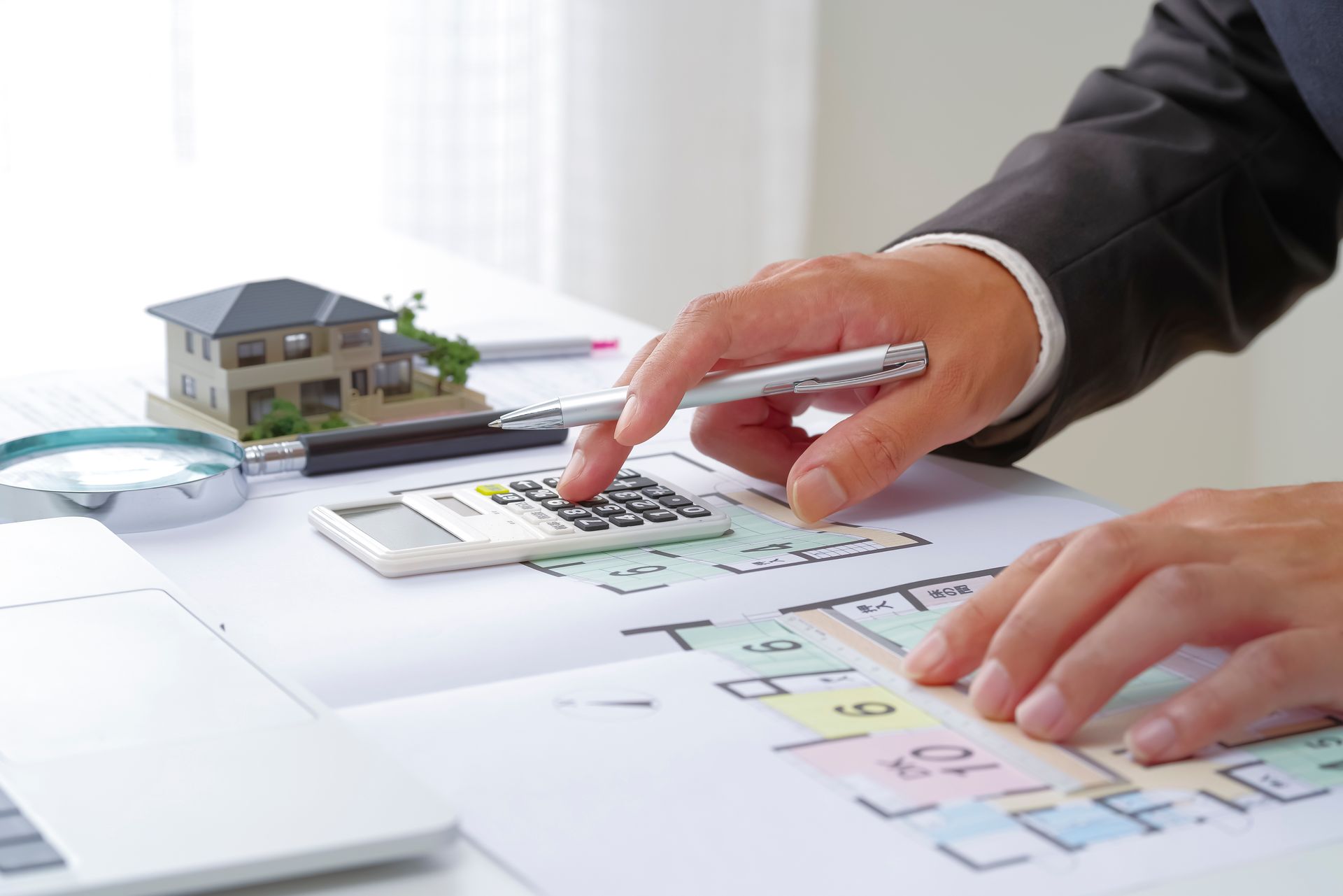 Une personne effectuant des calculs à la calculatrice sur des plans d'étage et une maison modèle.