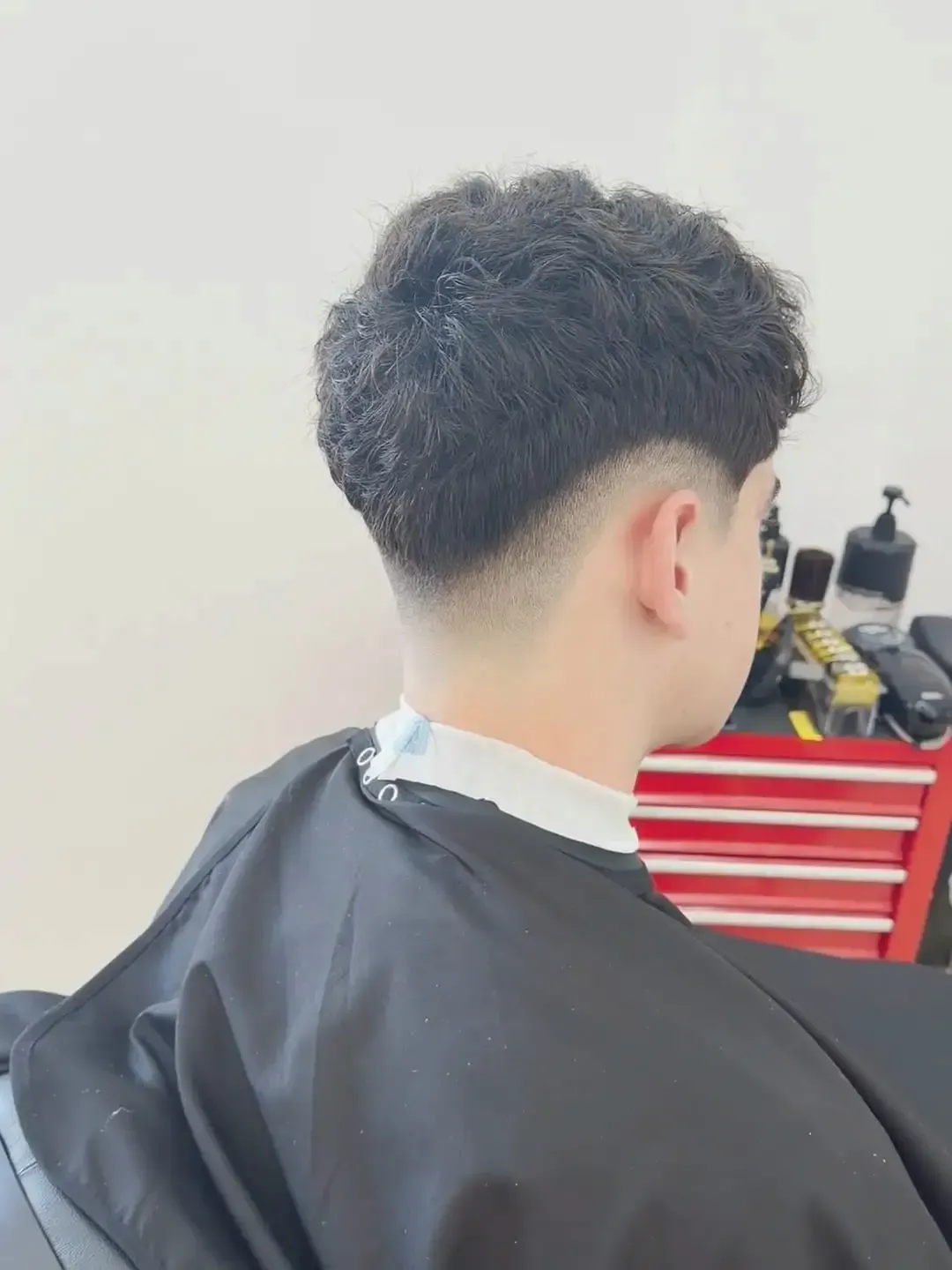 Parte posterior de la cabeza de una persona con el pelo corto y rizado, sentada en una silla de barbería