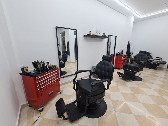Peluquería con sillones de peluquería negros, armario de herramientas rojo, espejos y suelo de baldosas a cuadros.