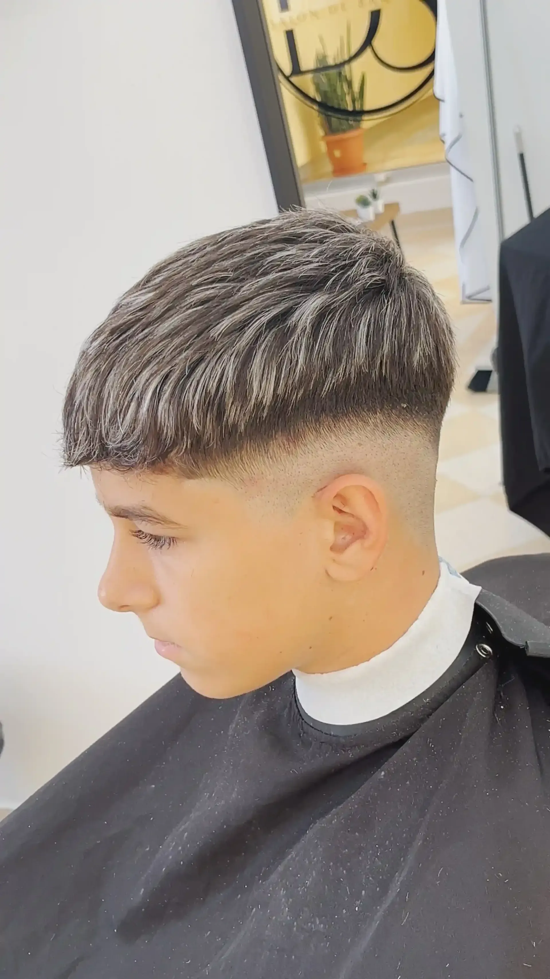 Corte de pelo de perfil con la parte superior texturizada y los laterales desvanecidos en una silla de barbero.