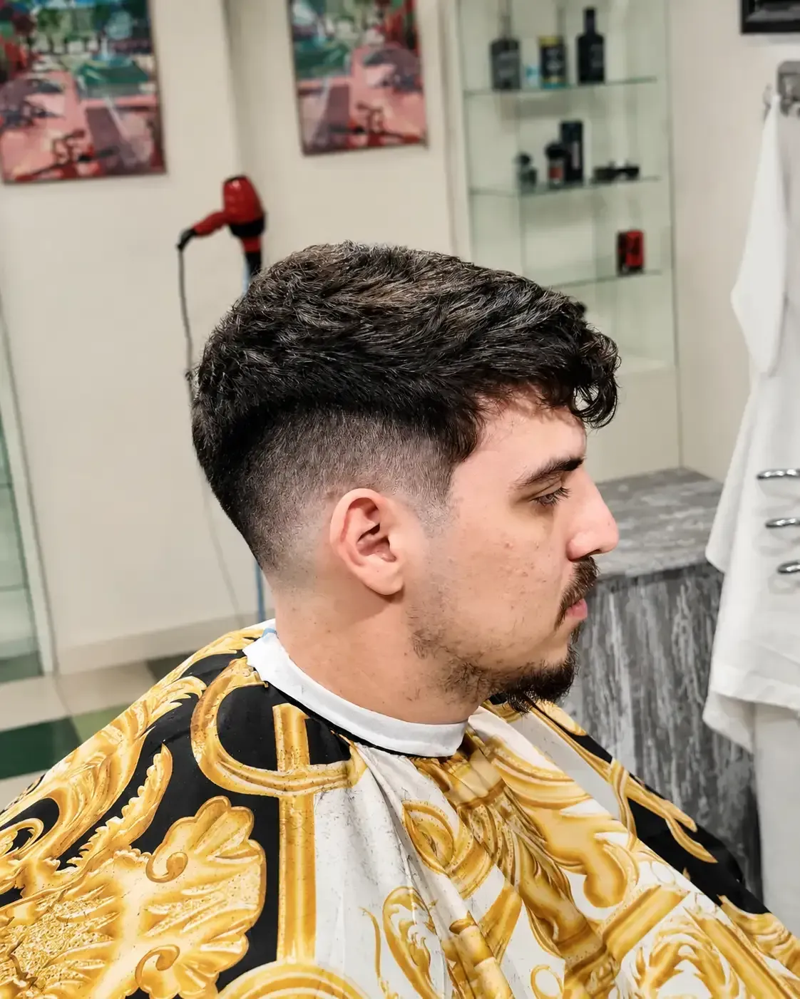 Corte de pelo de perfil en una barbería, con una capa con estampado dorado y un degradado limpio.