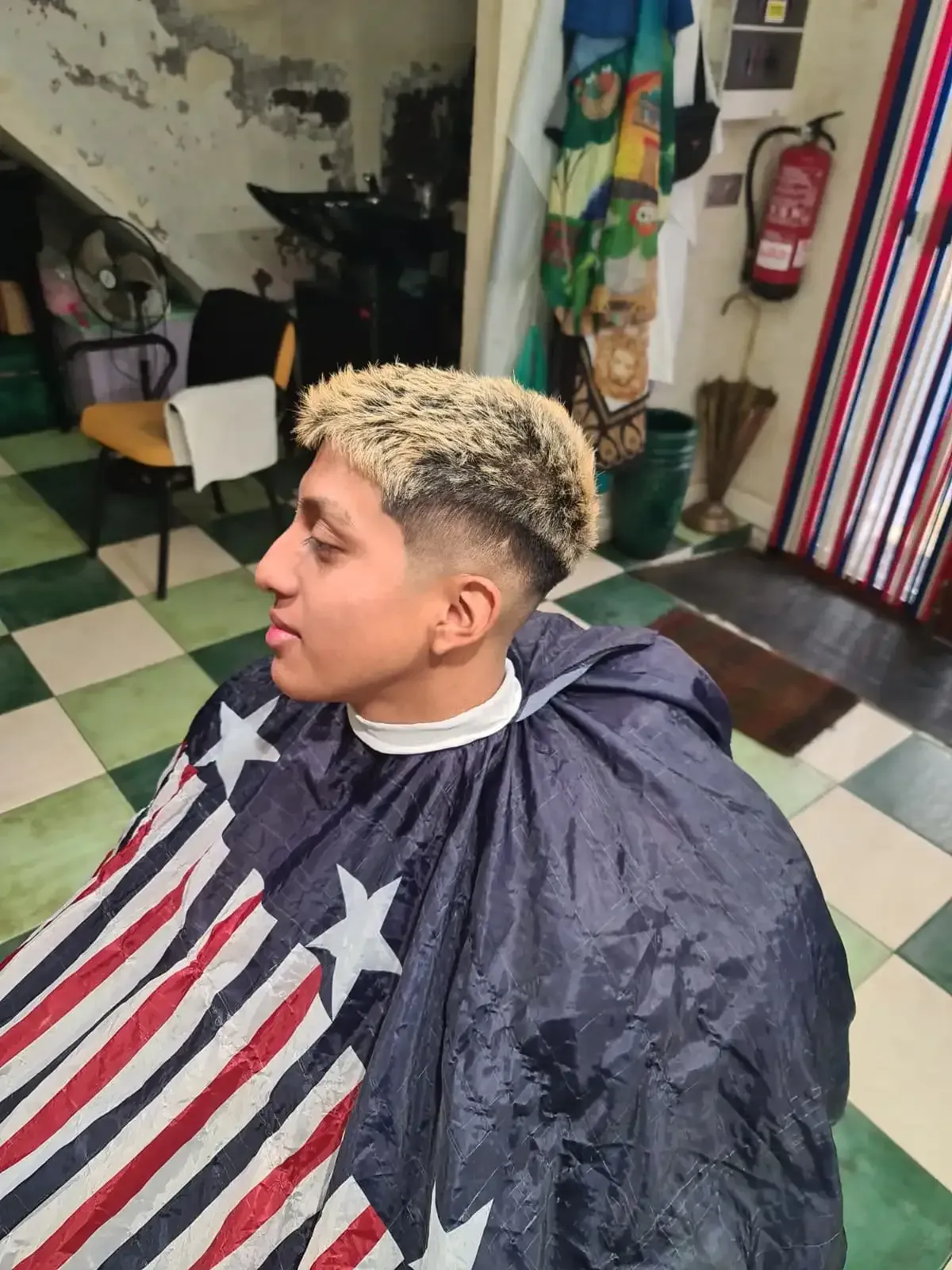 Una persona con el pelo rubio y corto está sentada en una silla de barbero