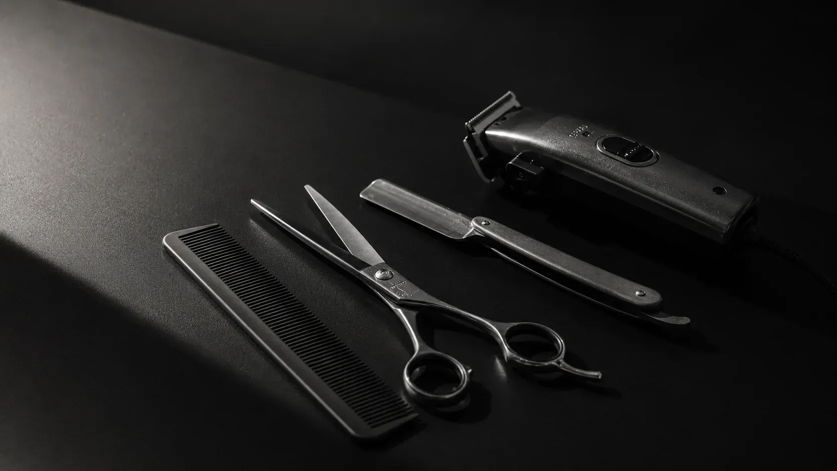 Kit de aseo negro con cortapelos, tijeras, peines y maquinilla de afeitar sobre una superficie oscura.