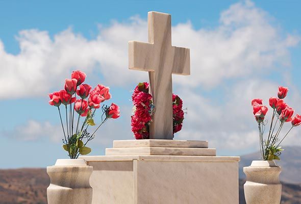 Un cementerio con una cruz y jarrones con flores rojas.
