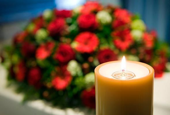 Se enciende una vela delante de un ramo de flores rojas.