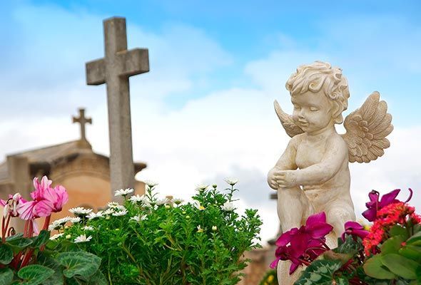 Hay una estatua de un ángel en primer plano y una cruz en el fondo.