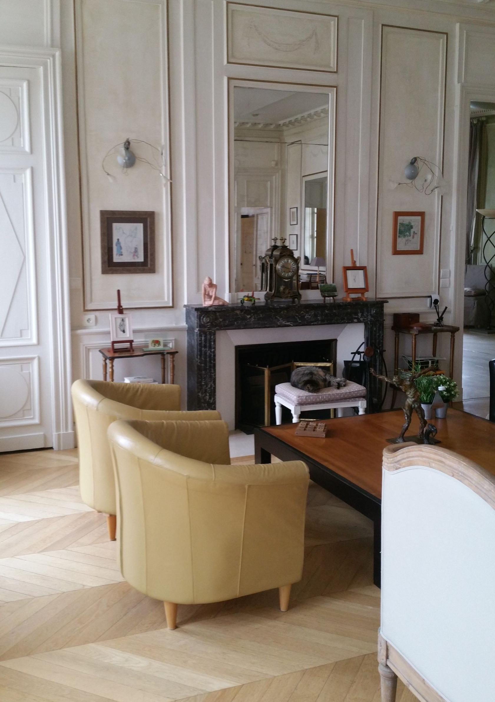 Salon avec fauteuils jaunes, cheminée, murs blancs ornés et parquet.