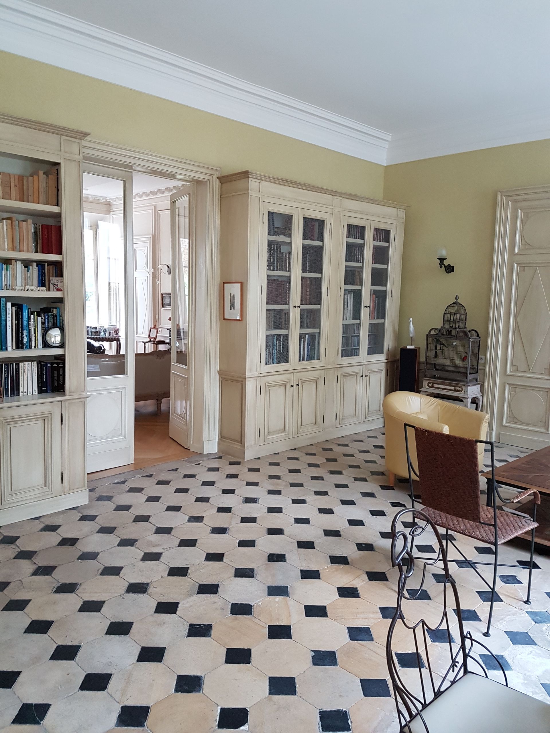 Pièce avec sol carrelé, bibliothèque intégrée et portes-fenêtres donnant sur une autre pièce.