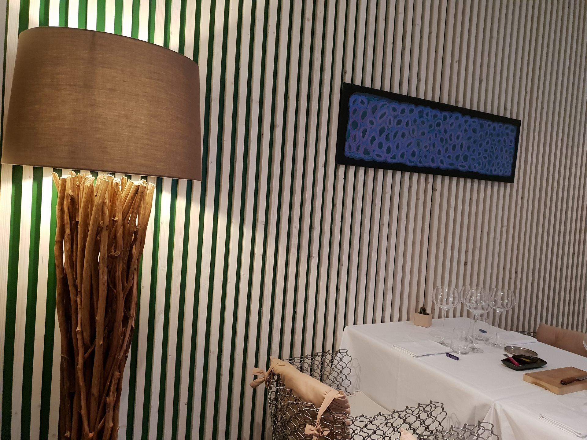 Lampe à pied texturé près d'un mur à rayures, d'une œuvre d'art rectangulaire bleue et d'une table dressée pour le repas.