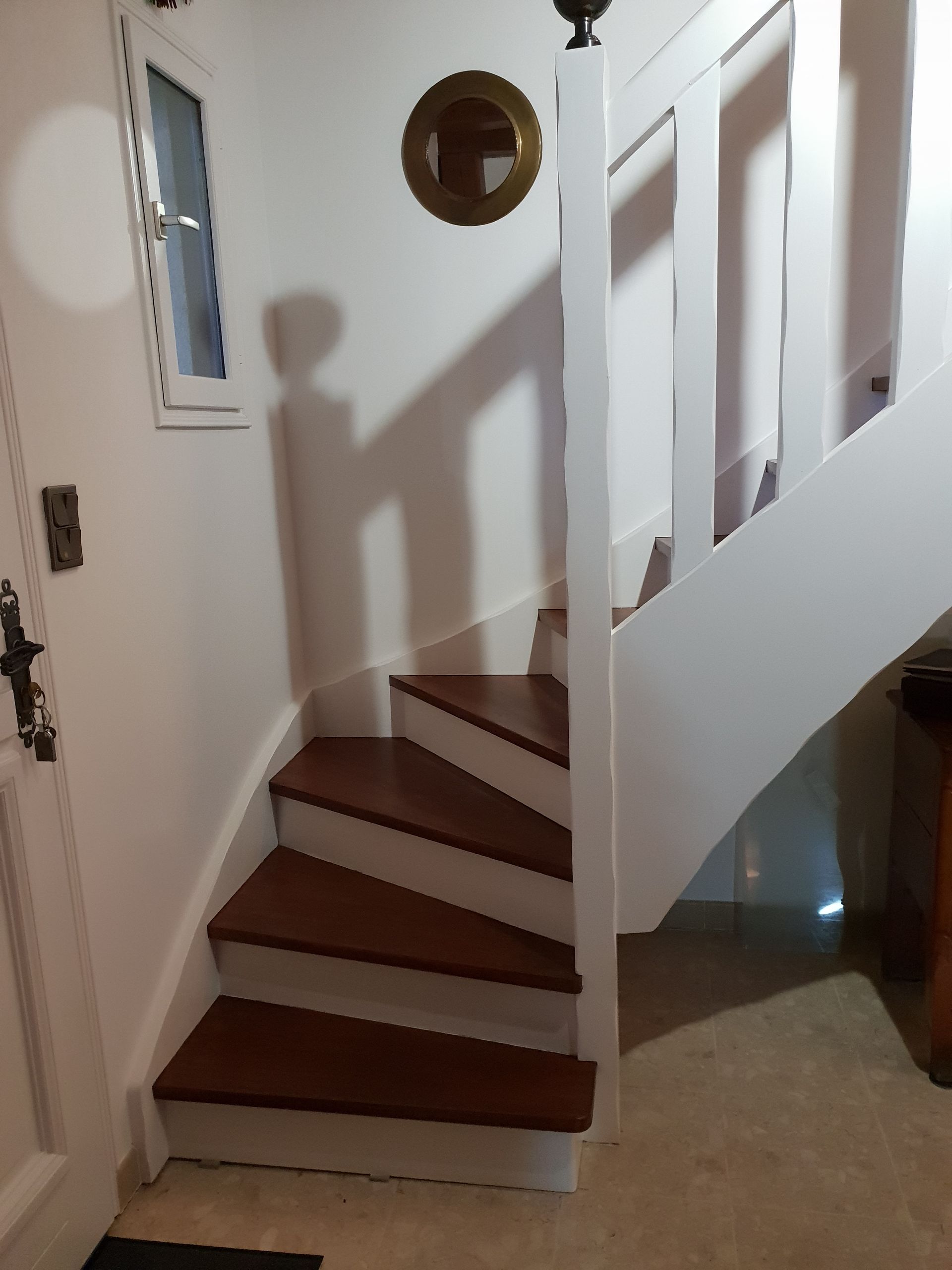 Escalier en bois avec rampe blanche, marches marron et une petite fenêtre sur la gauche.