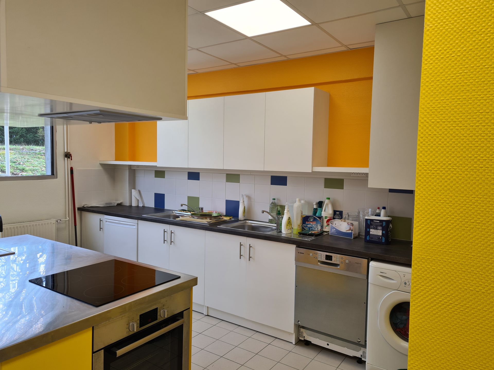 Cuisine avec armoires blanches, mur d'accent jaune et électroménagers en acier inoxydable.