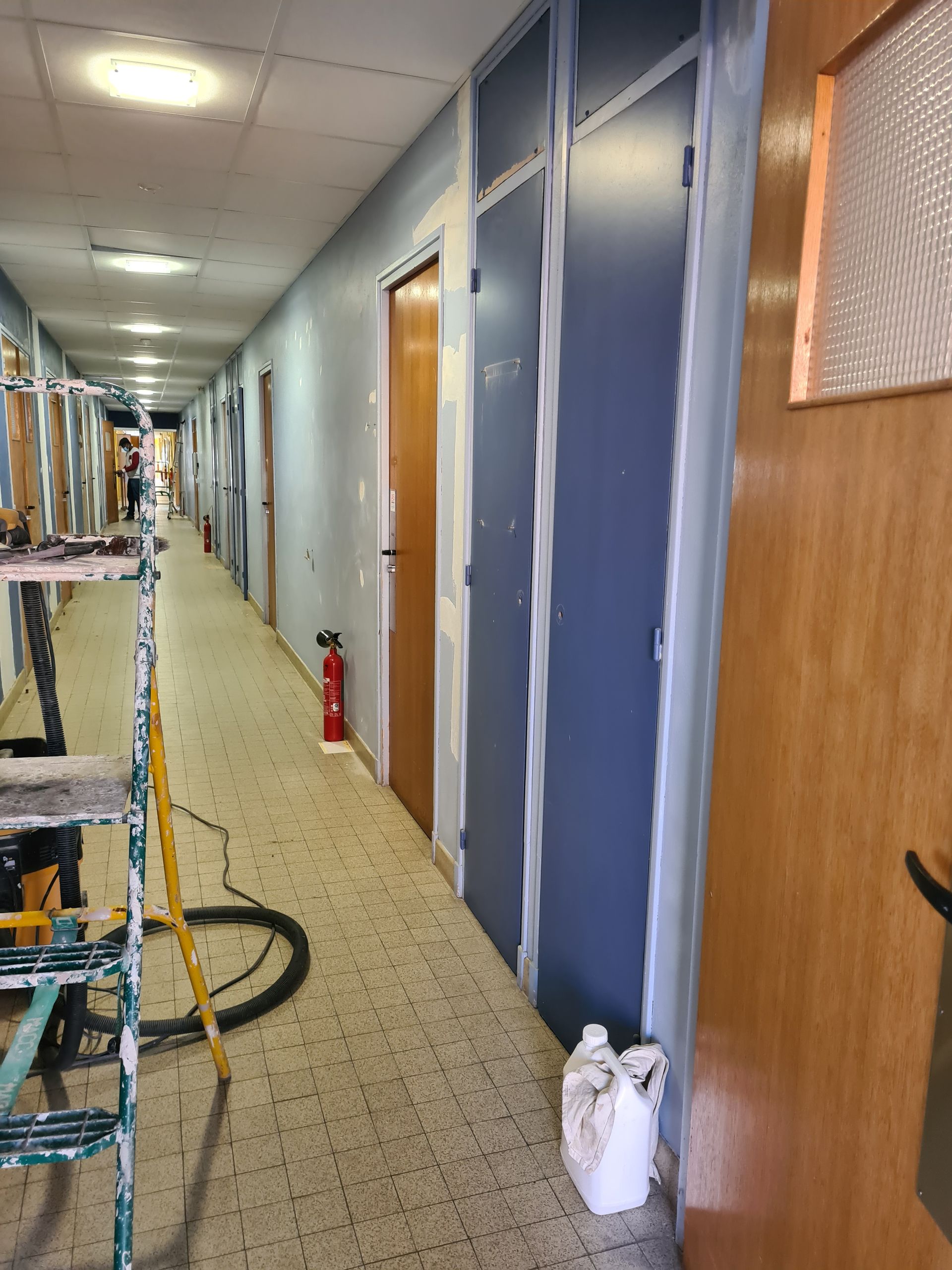Un long couloir est en cours de rénovation : portes, échafaudages et peinture.