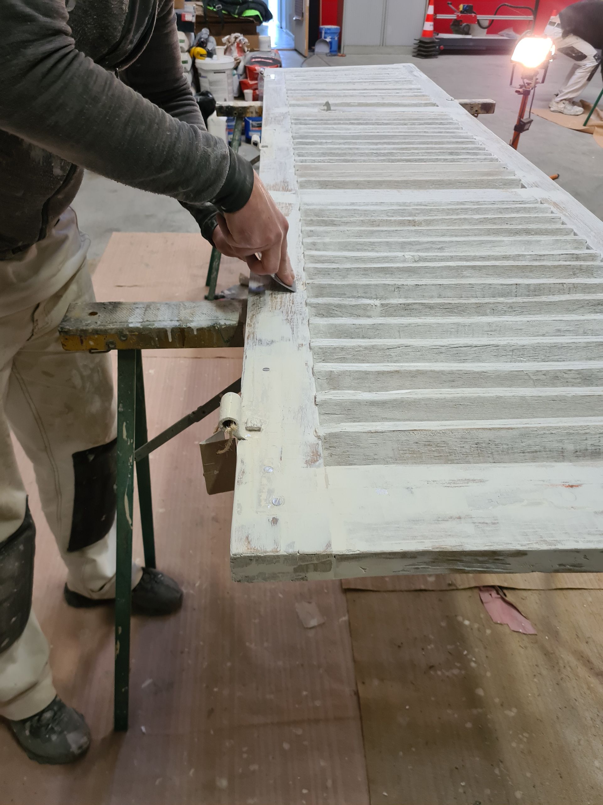 Personne ponçant un volet en bois sur un établi ; intérieur, bois clair.