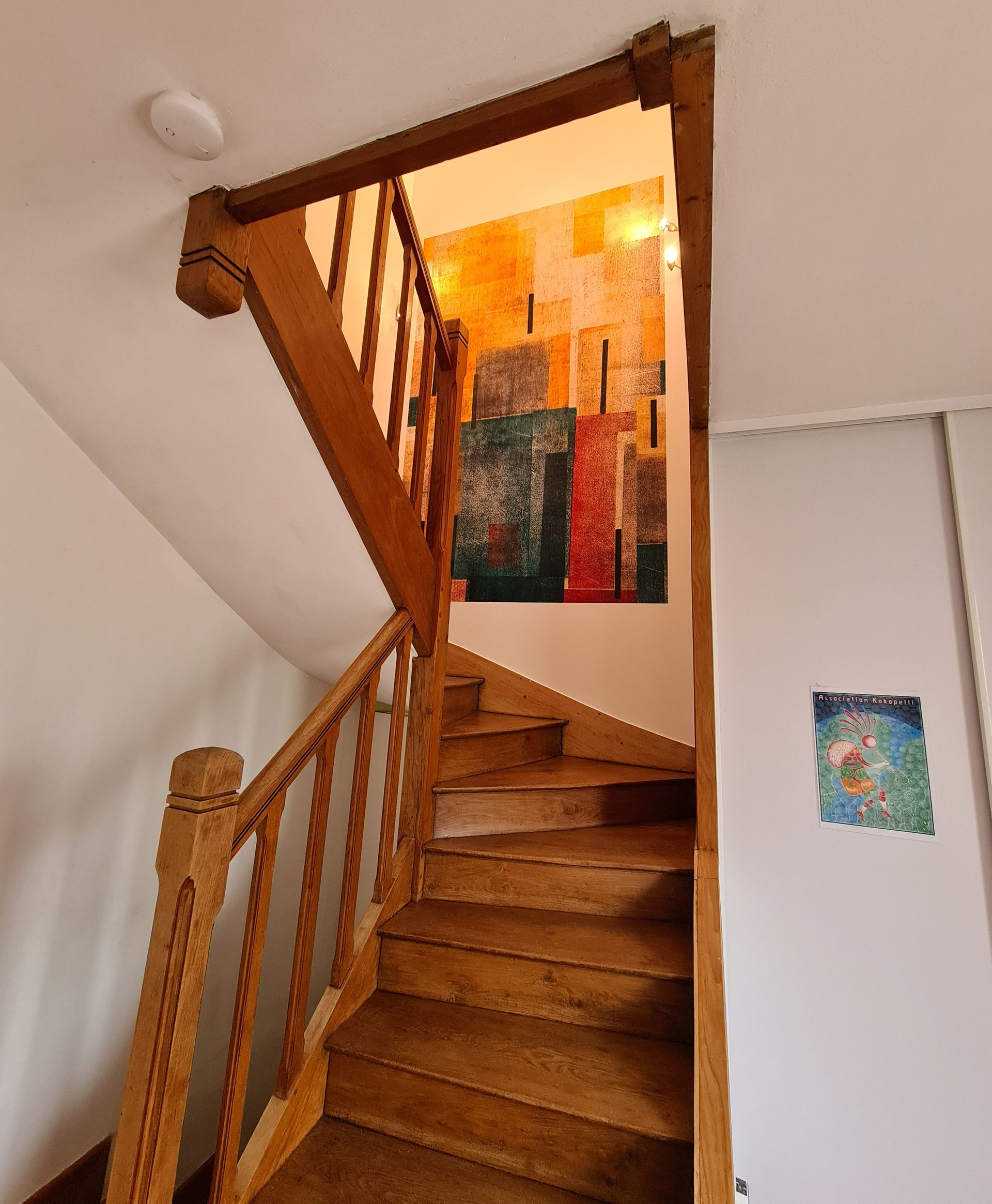 Escalier en bois avec rampe, vu d'en bas. Les marches sont claires et usées.