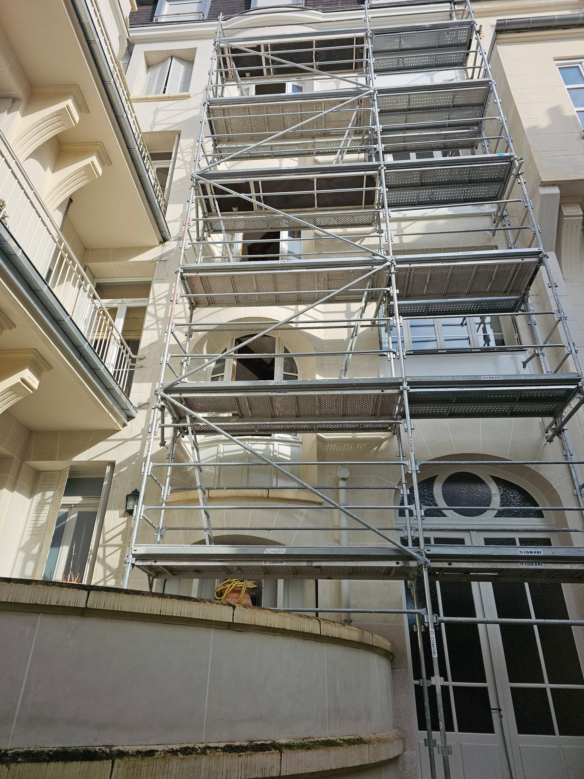 Échafaudages sur la façade d'un immeuble en rénovation. Plusieurs niveaux, certains occupés par des ouvriers.