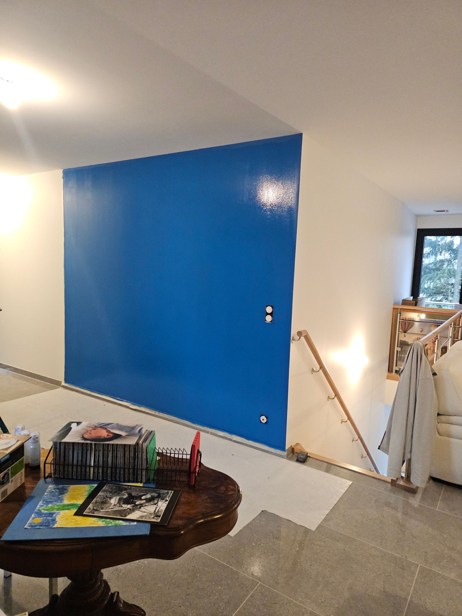 Porte bleue sur un mur blanc, dans un intérieur de maison avec escalier et table en bois.