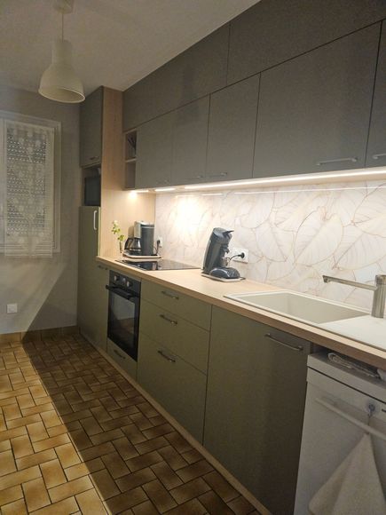Cuisine moderne blanche avec comptoirs en bois, four encastré et fenêtre donnant sur un immeuble.
