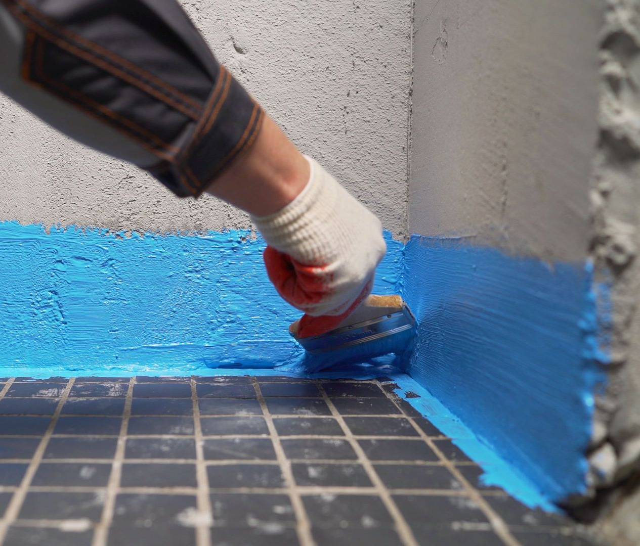 Personne appliquant du mastic bleu dans un coin à l'aide d'une truelle, portant un gant ; chantier de construction.
