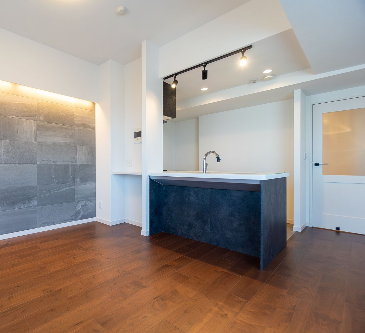 Cuisine moderne avec îlot central, mur d'accent en carrelage gris, parquet foncé et éclairage encastré.