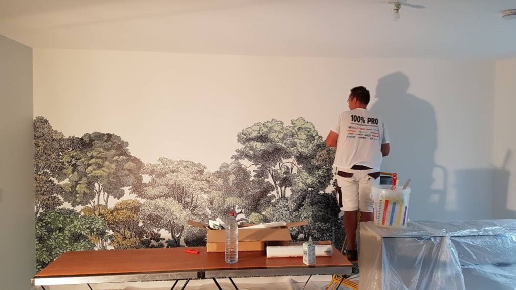 Une personne peignant une fresque murale représentant une scène de forêt.