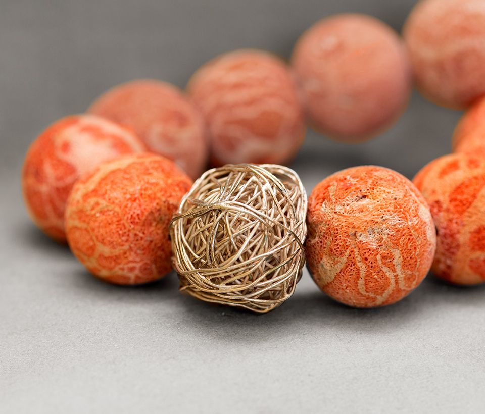 Orangefarbene Korallenperlen mit einer Kugel aus Golddraht auf grauem Untergrund.