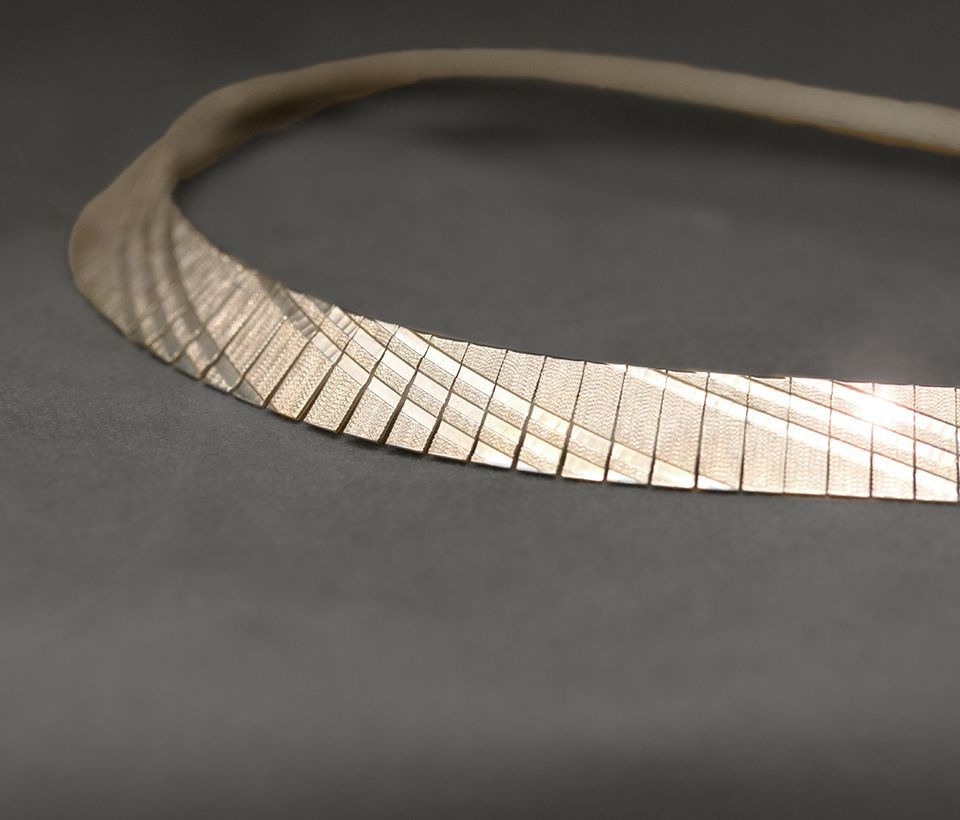 Silberne Halskette mit Fischgrätenmuster auf grauer Oberfläche.