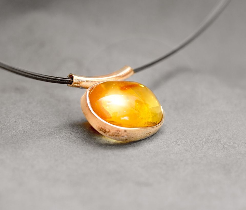 Bernstein-Anhängerkette mit goldfarbener Fassung auf grauem Untergrund.