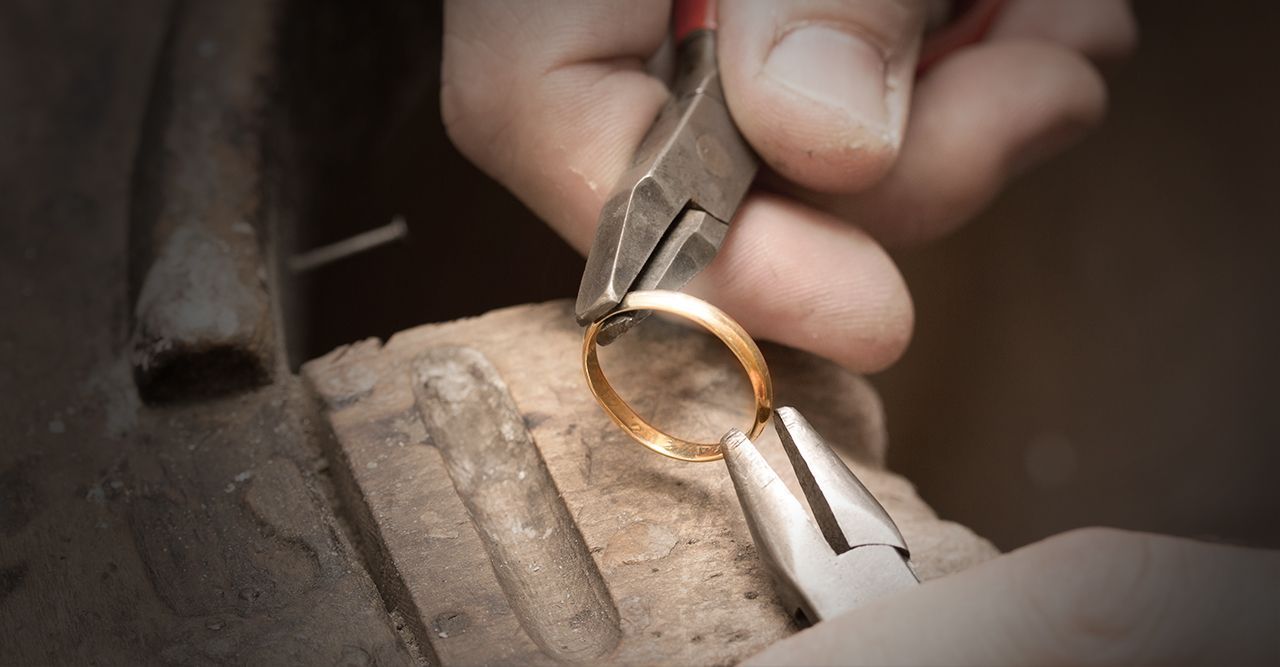 Eine Person verwendet eine Zange, um einen Goldring auf einer hölzernen Werkbank anzupassen.