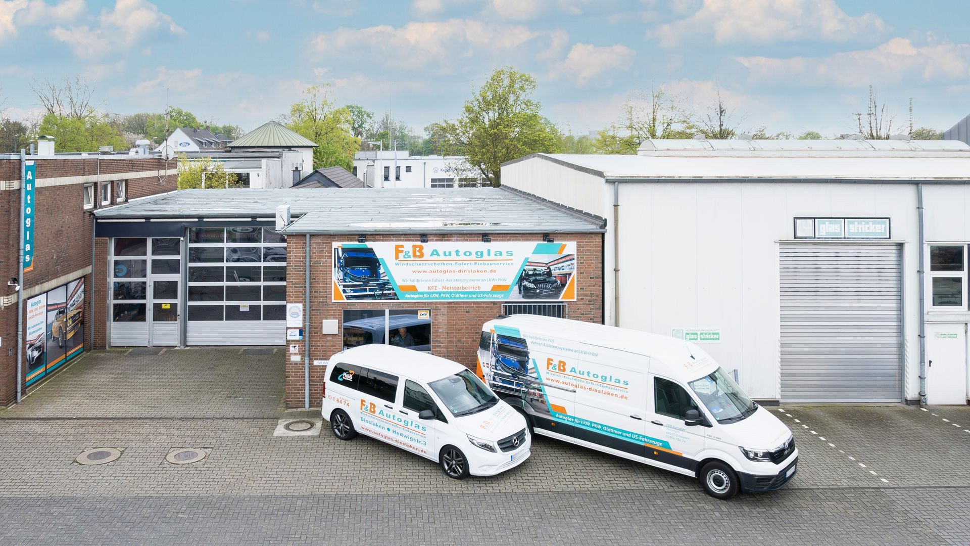 Zwei weiße Lieferwagen stehen vor einem Gebäude mit einem Banner für fb autoglas