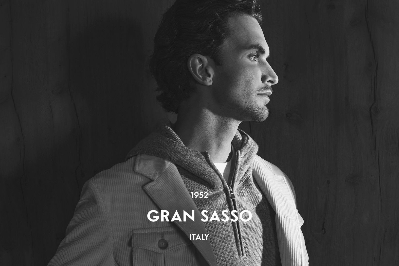 Homme en blazer et sweat-shirt à capuche, regardant hors champ. Inscription GRAN SASSO ITALY en dessous.