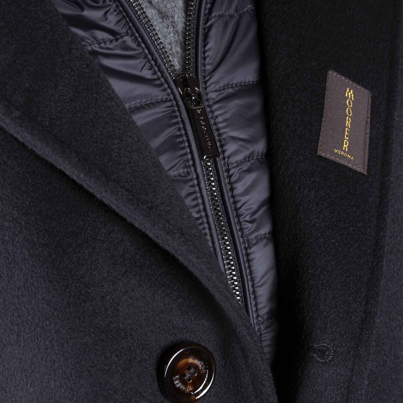 Gros plan sur un manteau en laine bleu marine à intérieur matelassé noir. Un bouton est visible.