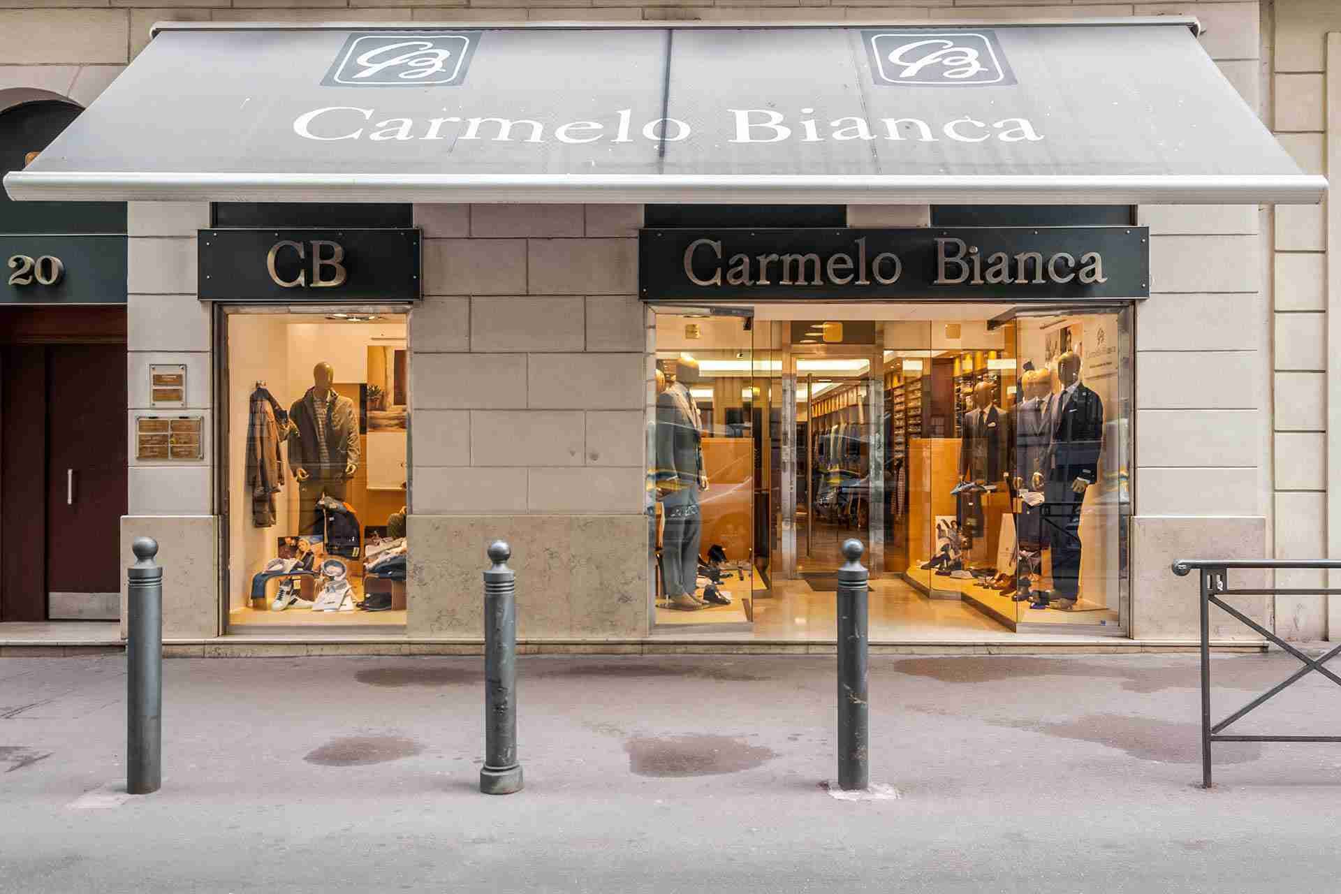 Façade du magasin Carmelo Bianca avec auvent ; vitrines présentant des vêtements et des mannequins ; dans une rue de la ville.