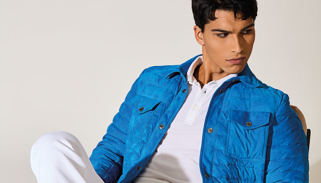 Homme en veste bleue et polo blanc, assis, regardant vers le bas.