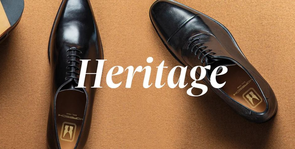 Deux chaussures Oxford en cuir noir sur une surface marron, avec le mot Heritage.