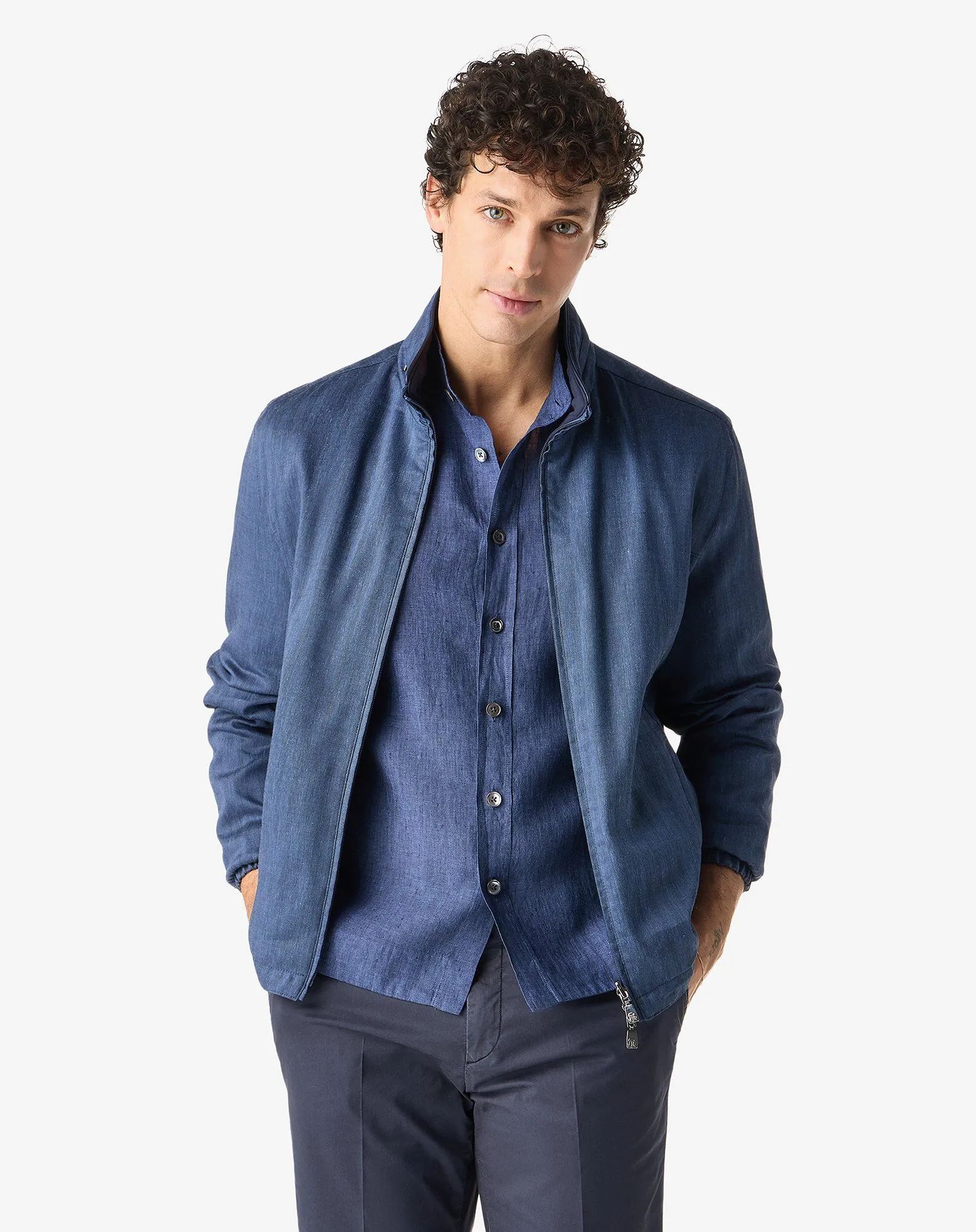 Personne portant une veste et une chemise bleues, les mains dans les poches, se détachant sur un fond blanc.