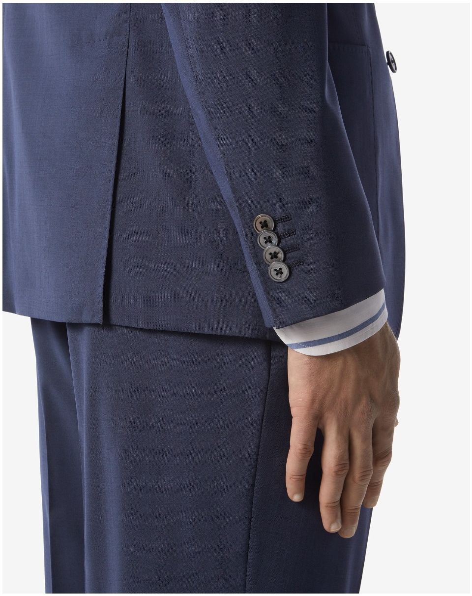 Homme en costume bleu, montrant ses poignets boutonnés et une chemise rayée en dessous.