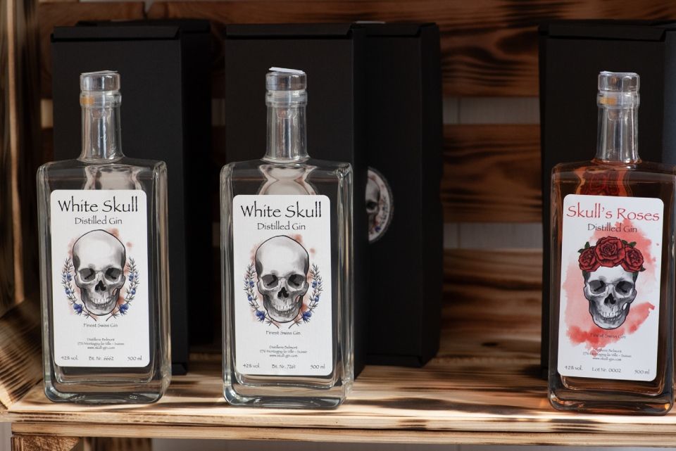 Trois bouteilles d'alcool avec des étiquettes à tête de mort sur une étagère en bois ; deux gins « White Skull », un gin « Skull's Revenge ».