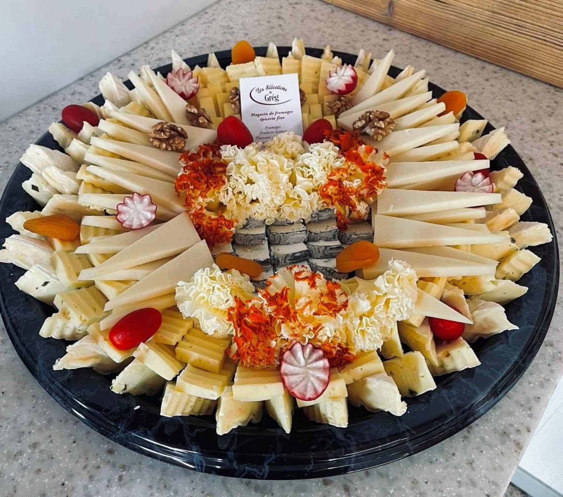 Plateau de fromages variés, accompagné de fruits et de noix, présenté sur une assiette foncée.
