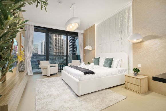 Modern bedroom with a white bed, large windows, and city views.