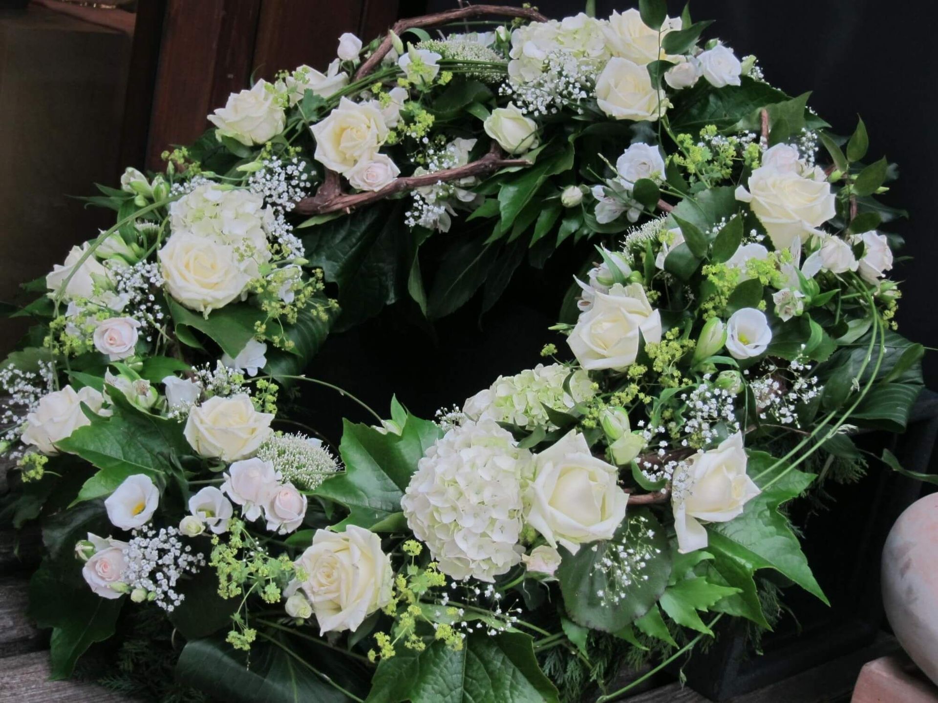 Trauerkranz mit weißen Rosen, Schleierkraut und grünen Blättern in klassischer Floristik.