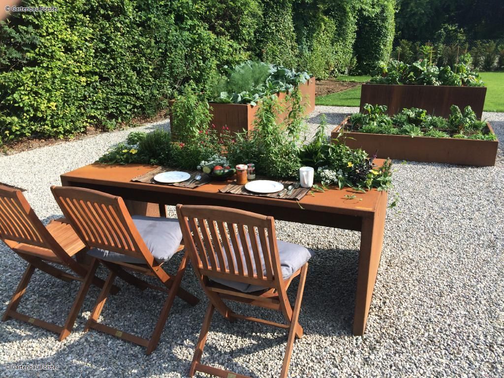 Tisch mit Stühlen vor mehreren Hochbeeten