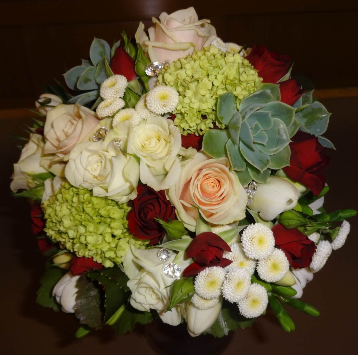 Kompakter Brautstrauß mit weißen Rosen, Sukkulenten und zarten roten Akzenten.