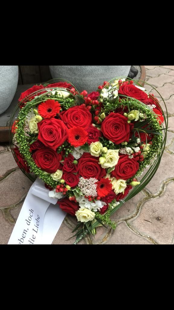 Trauergesteck mit roten Rosen und grünen Blättern vor Steinvasen.