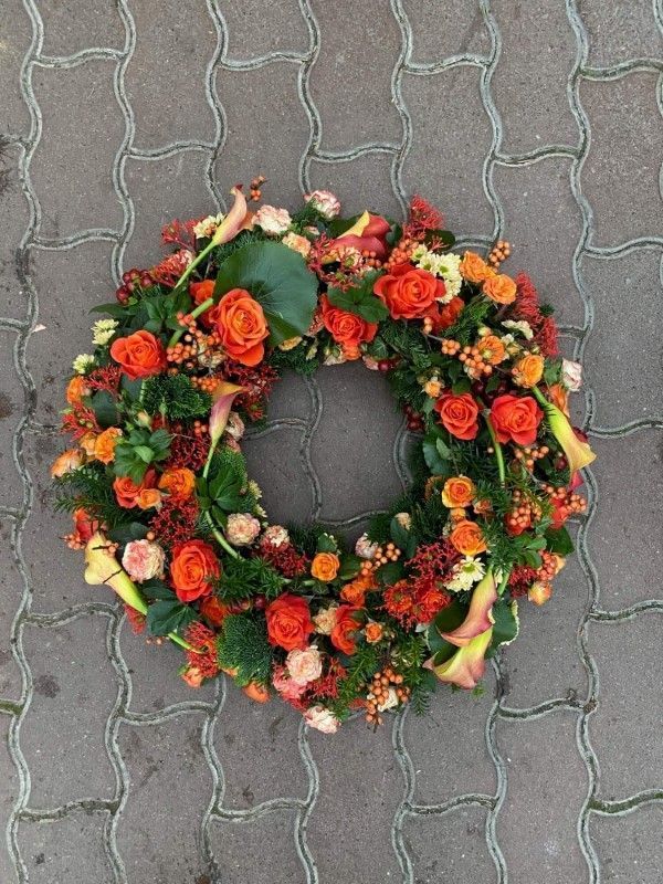 Trauerkranz in Orange und Rot mit Rosen, Chrysanthemen und Beeren.