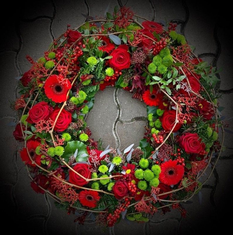 Runder Trauerkranz in kräftigem Rot und Grün mit Gerbera, Rosen und Beeren.