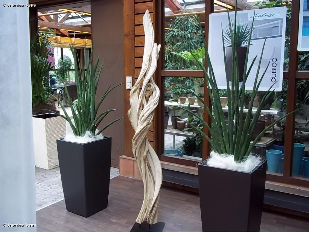 kunstvolle Skulptur zwischen zwei großen Topfpflanzen