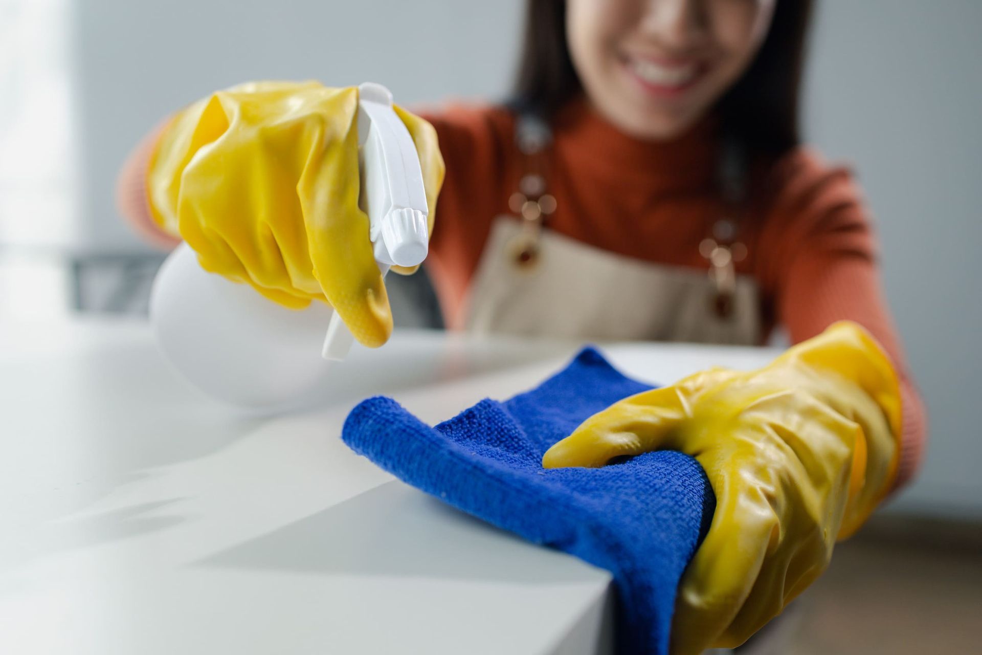 Una mujer que lleva guantes amarillos está limpiando un mostrador con un paño y una botella de spray.