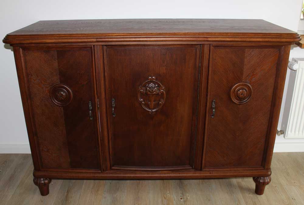 Holzschrank mit drei Türen, geschnitzten Details, dunkelbraun, auf kurzen Beinen stehend.