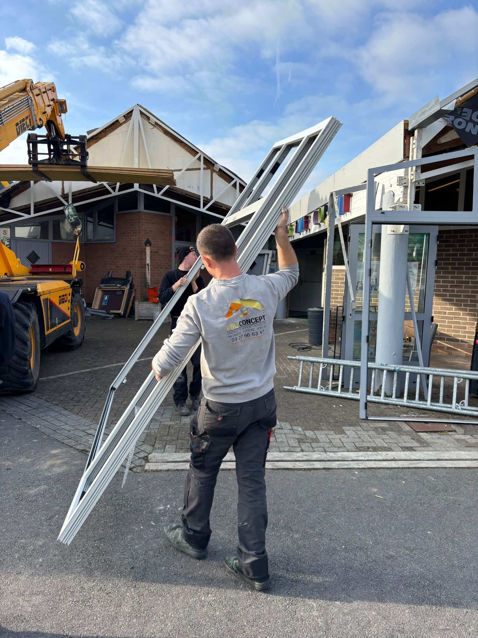 Un homme portant un grand cadre de fenêtre argenté à l'extérieur d'un bâtiment en construction.